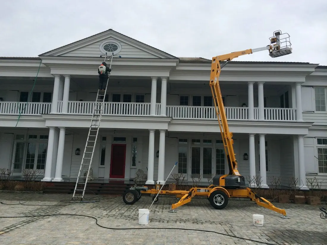 Fabian’s crew on a lift cleaning the second-floor windows of a columned Long Island home